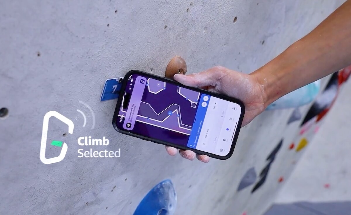 A hand holding a phone close to an NFC tag on a climbing wall, with the Griptonite app showing 'Climb Selected'